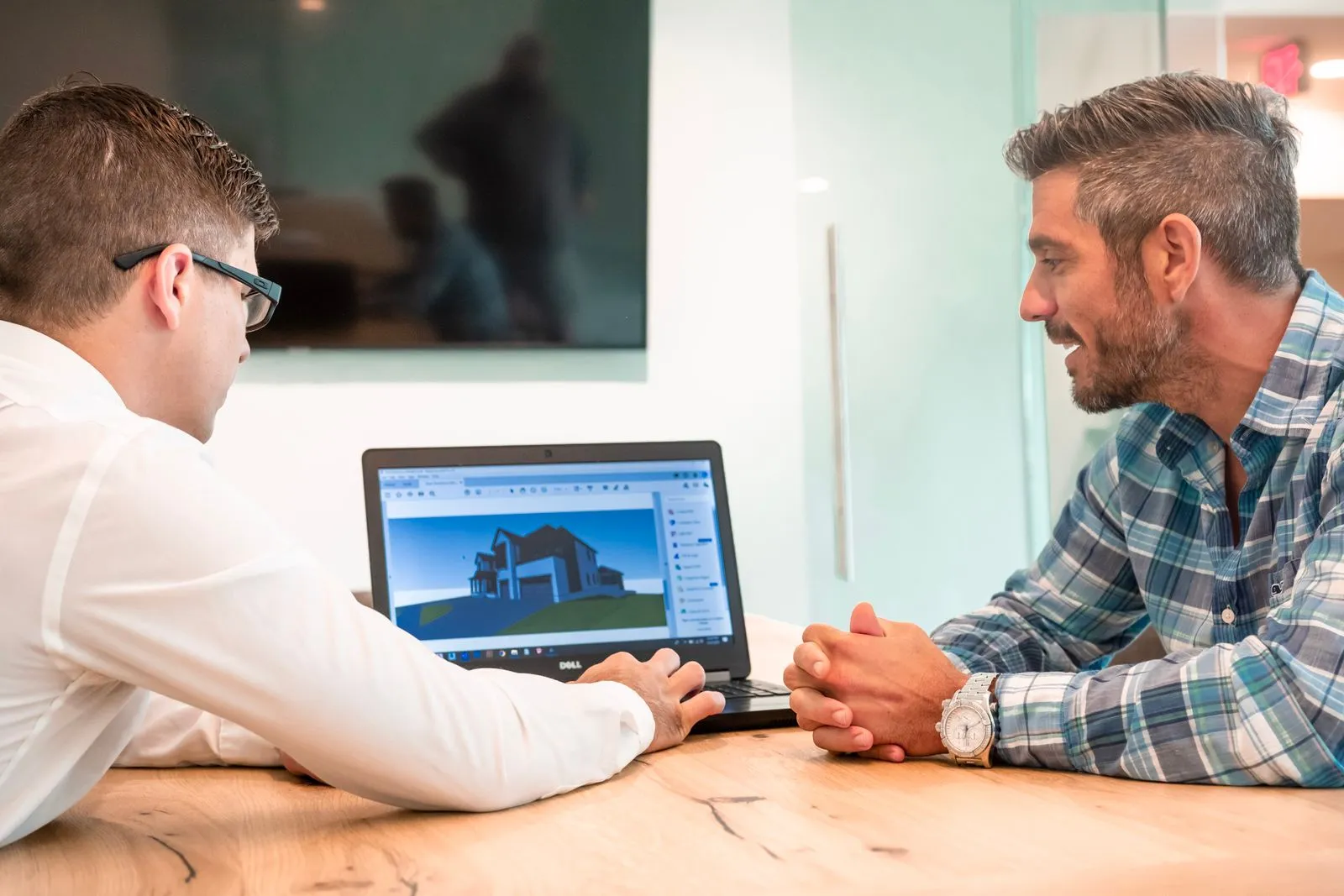 Two people discussing a 3D house model on a laptop