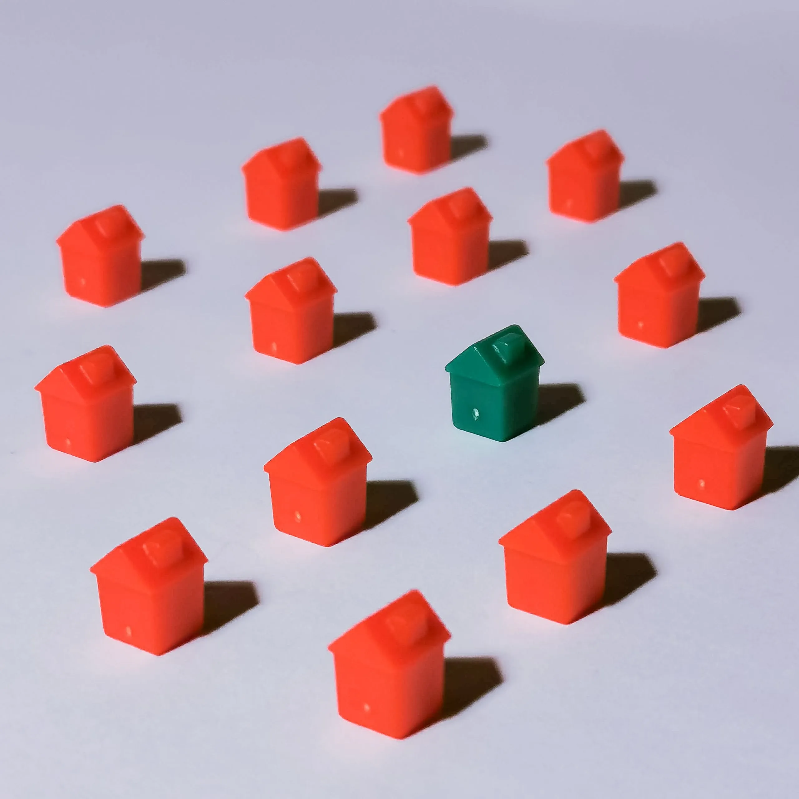 One green model house standing out in the centre of a ring of red ones on a plain white surface