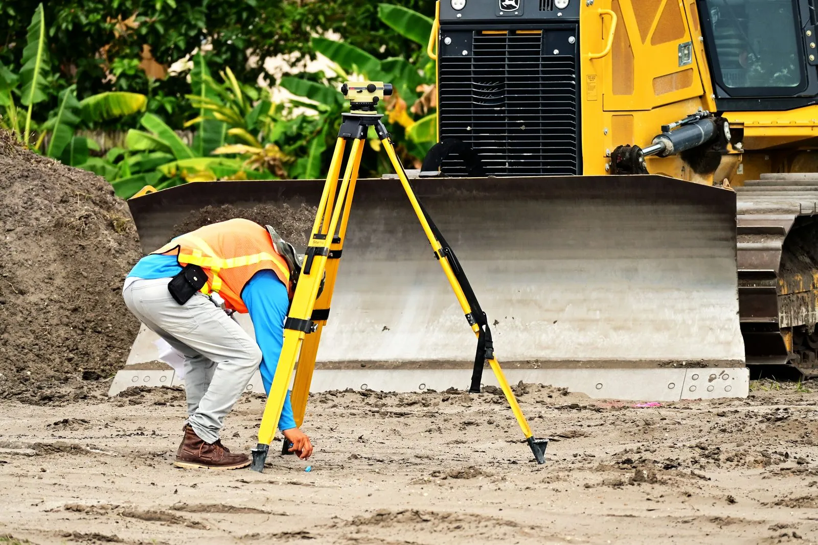A surveyor setting up a measuring instrument on a tripod at a construction site